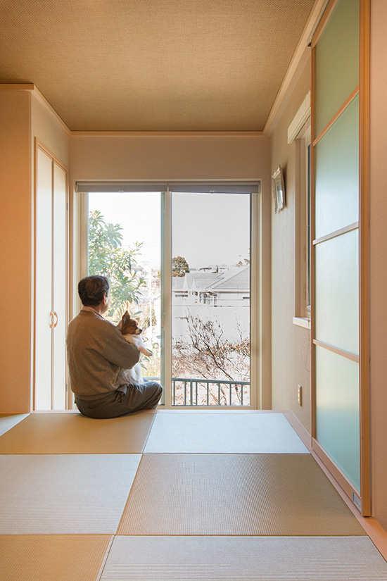 和室の窓から外の景色を眺める夫と犬