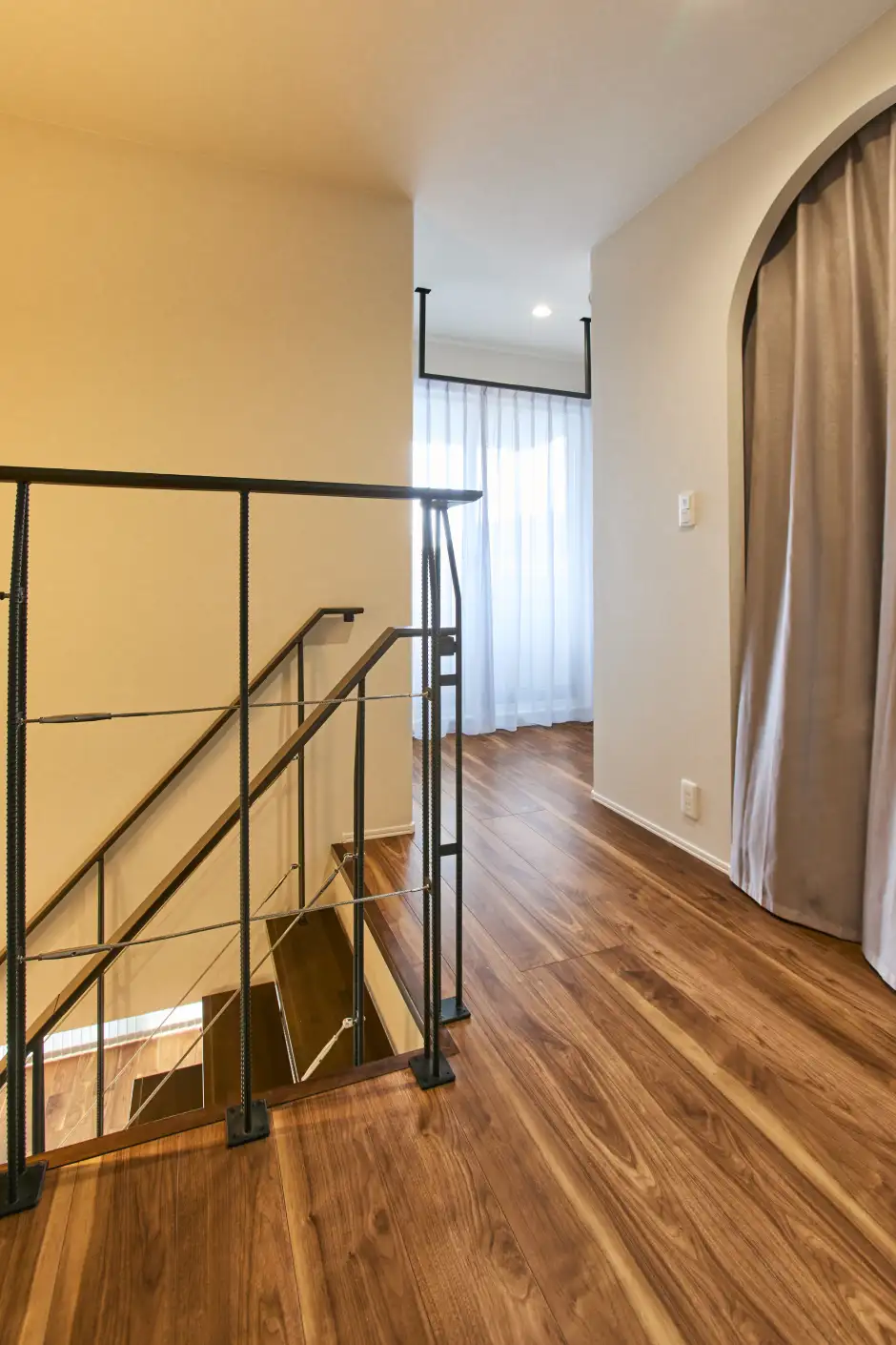 ウッドフロアの廊下にあるアーチ付きの入口とカーテンで区切られた2階ホール