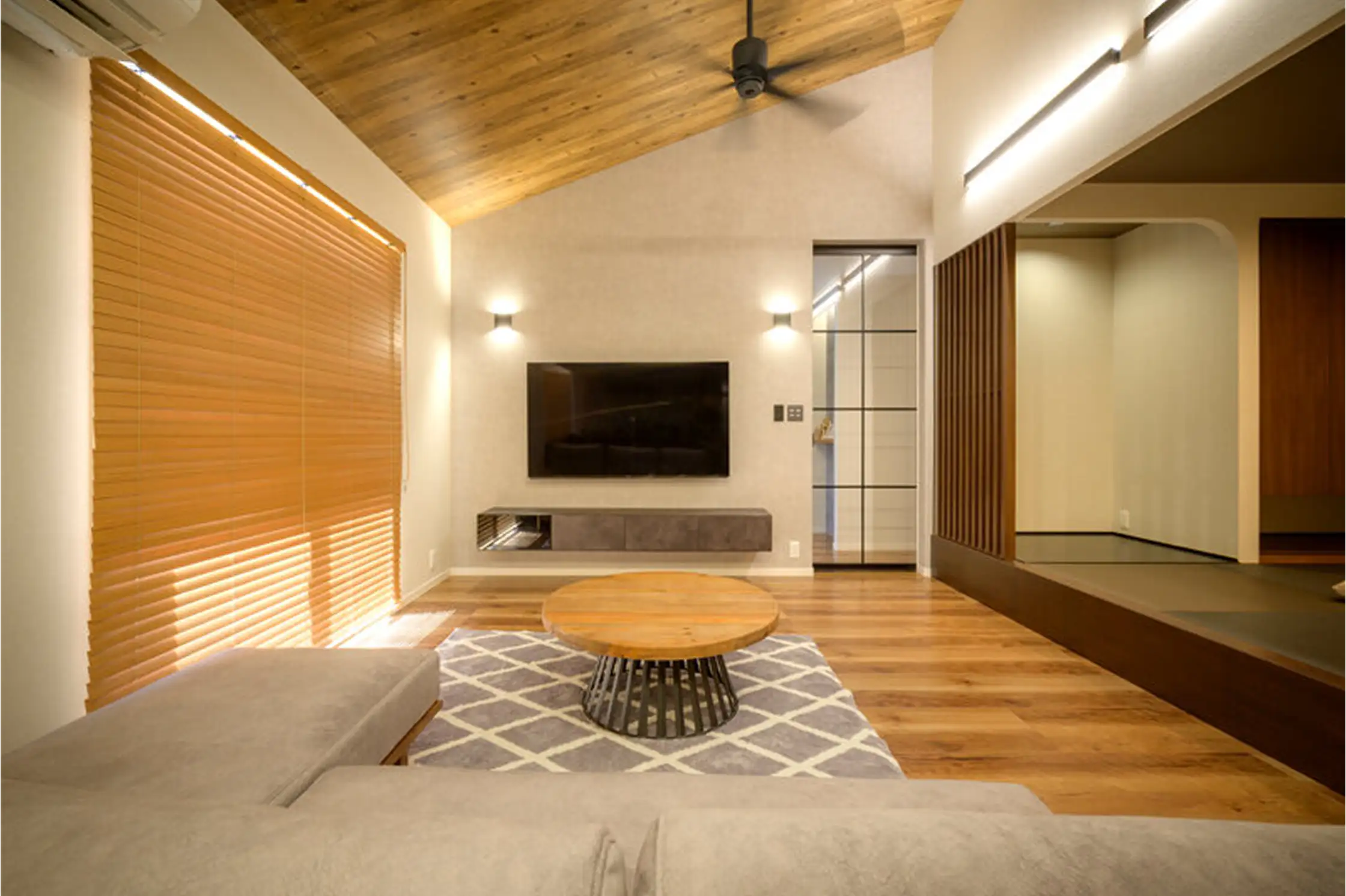 壁掛けTVとローテーブル、L字型ソファが置かれた開放的で明るいリビング