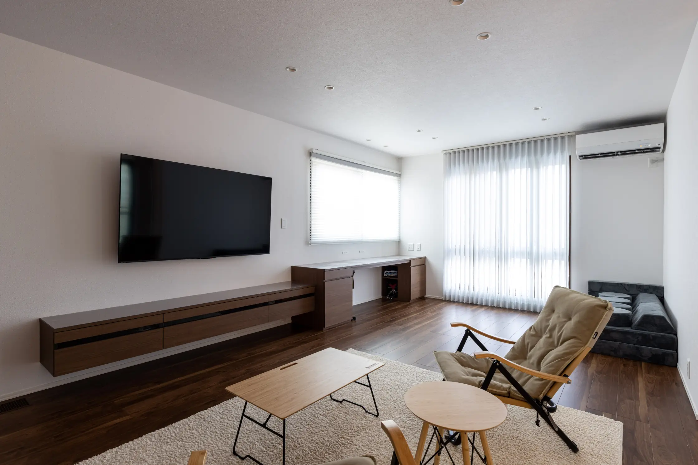 壁掛けTVと収納カウンターとアウトドアチェアとローテーブルがあるリビング