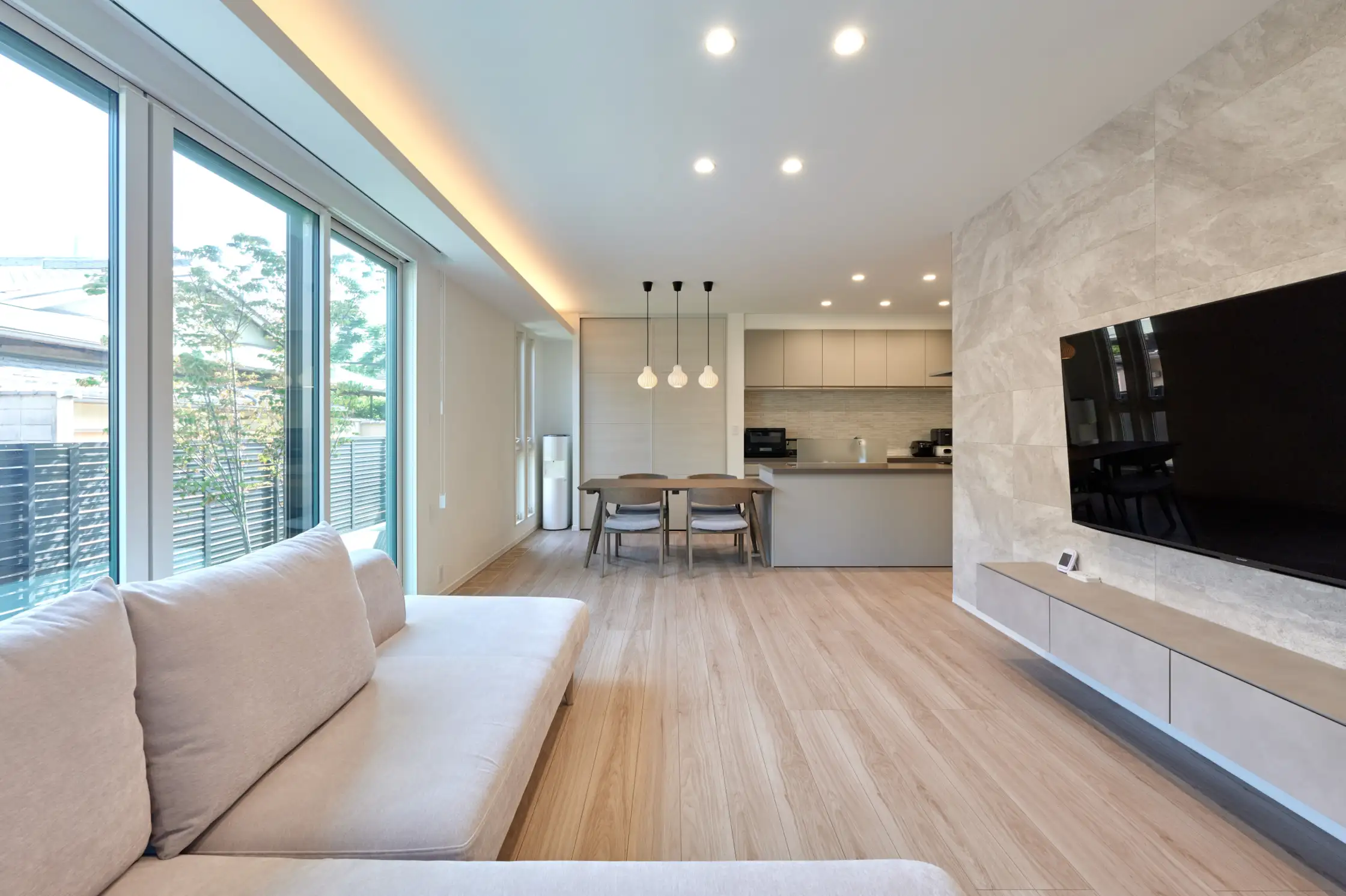 明るいリビングのすみに壁掛けテレビとソファが置かれている様子