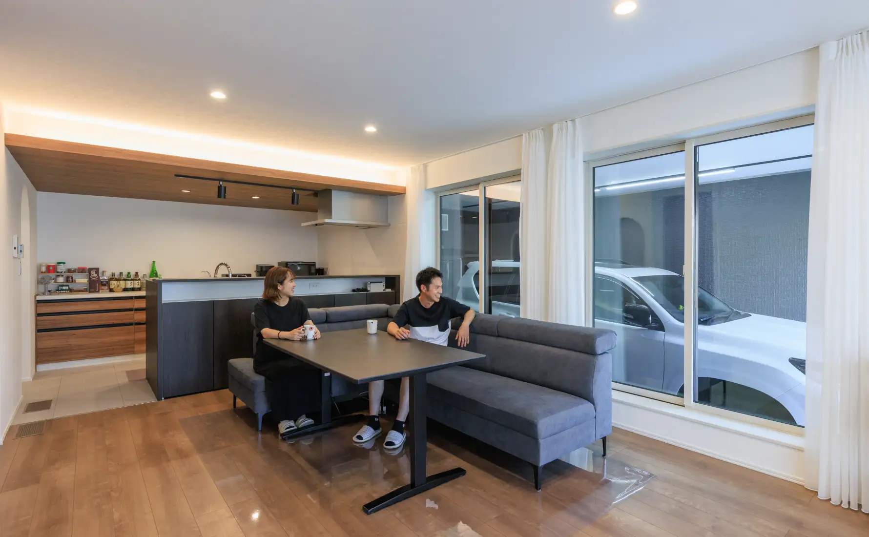 ご夫婦がリビングでくつろぎながらビルトインガレージの愛車を眺めている様子