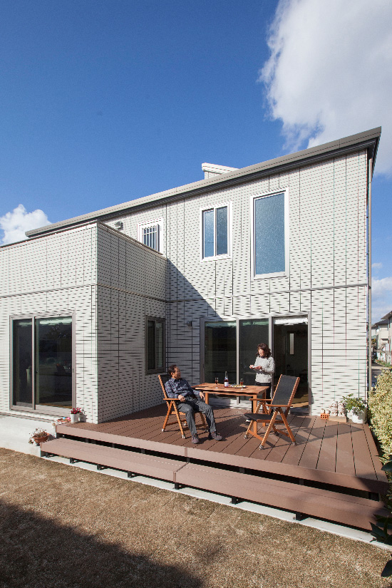 テーブルとチェアを置いた広いウッドデッキでくつろぐ夫婦