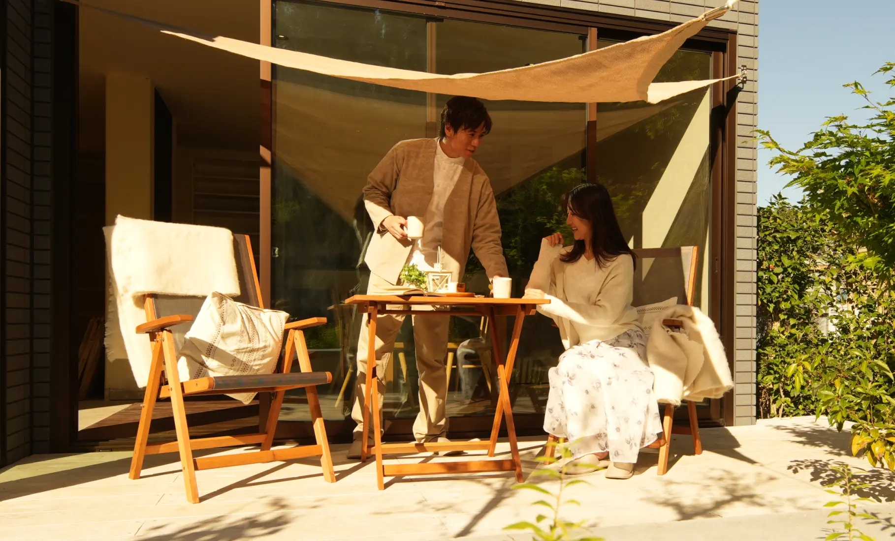 タープを張ったテラスの下で会話する夫婦