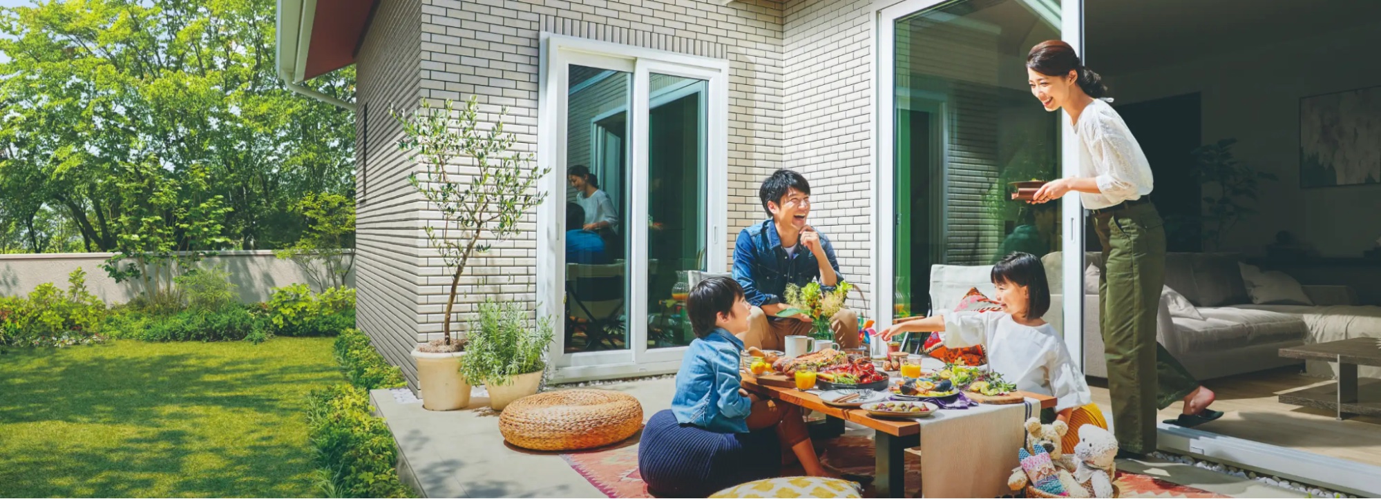 緑に囲まれた平屋の庭のテラスで家族が食事をたのしむシーン