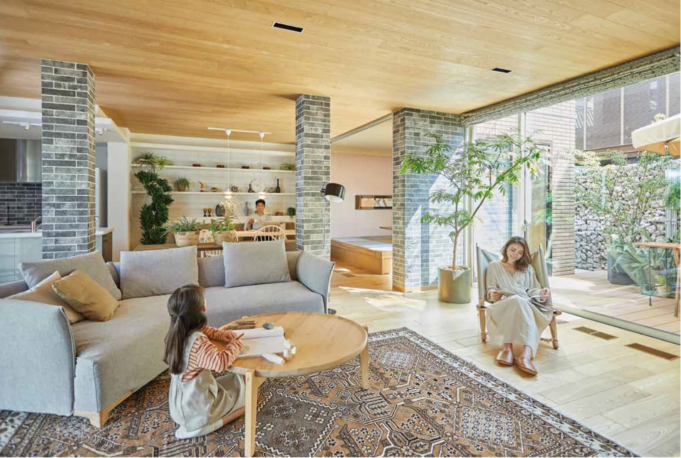 植栽のあるテラスを望む大開口を備えたリビングで、くつろぐ親子