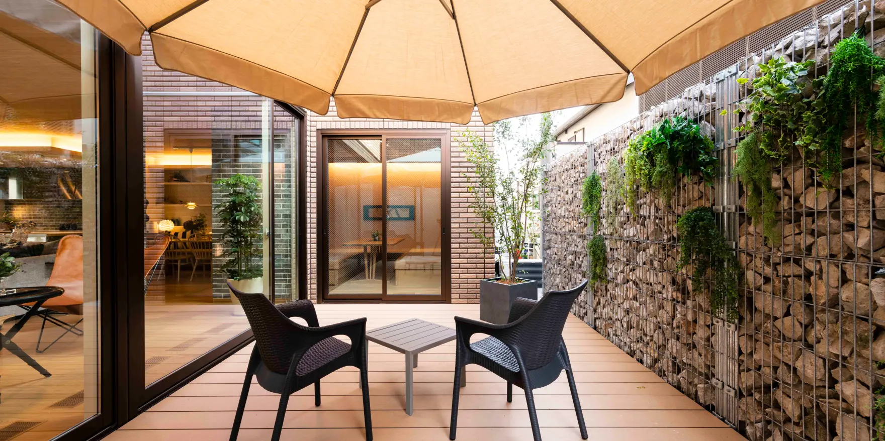 石組みの壁に囲まれた、ウッドデッキとパラソルのあるリゾート風の中庭