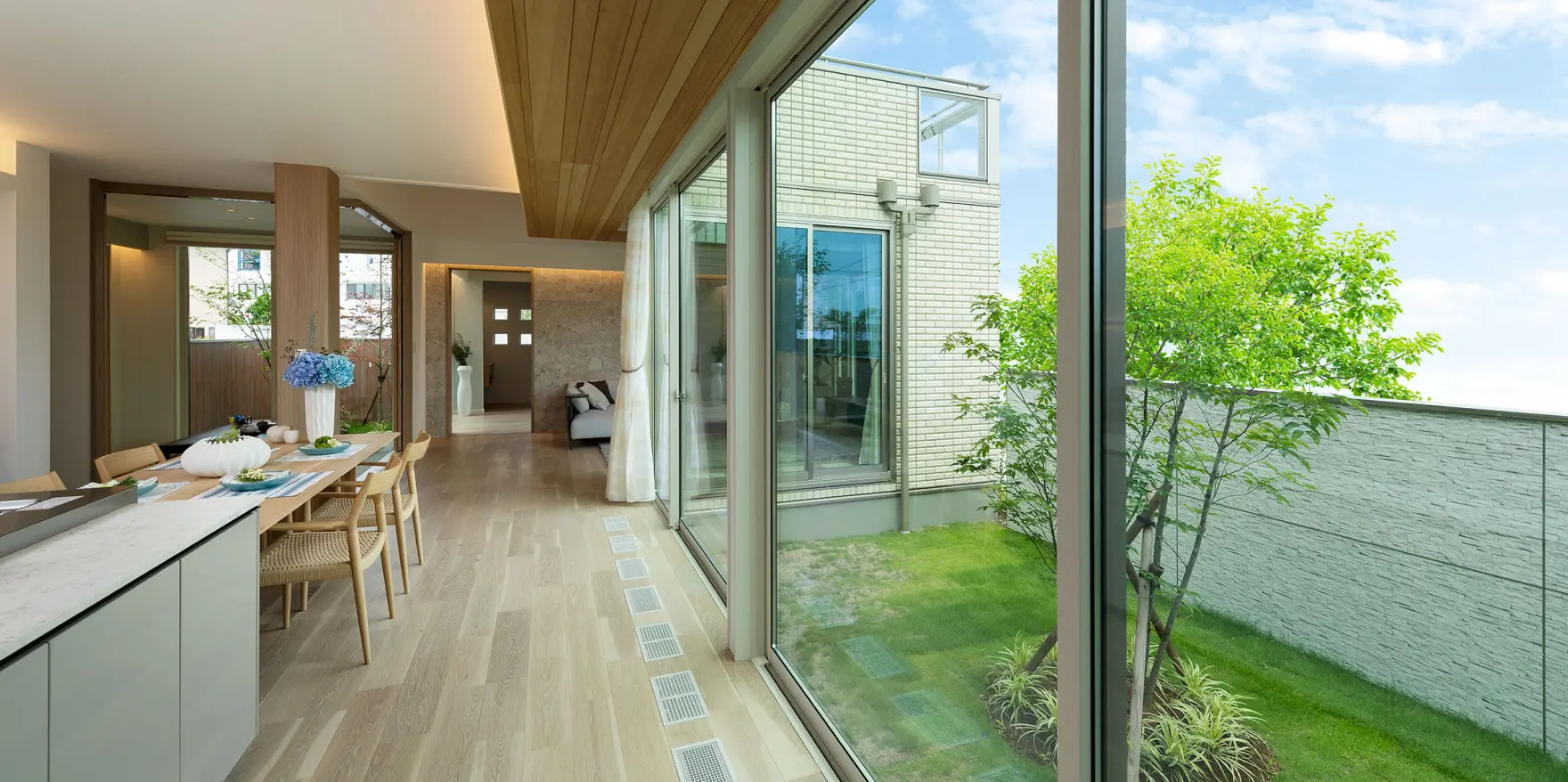LDKの大きな窓越しに眺める、芝生と植栽のある明るい中庭