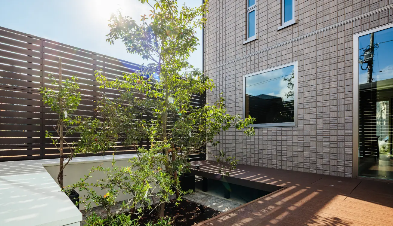 ルーバーフェンスで囲まれた、ウッドデッキと植栽のある明るい中庭