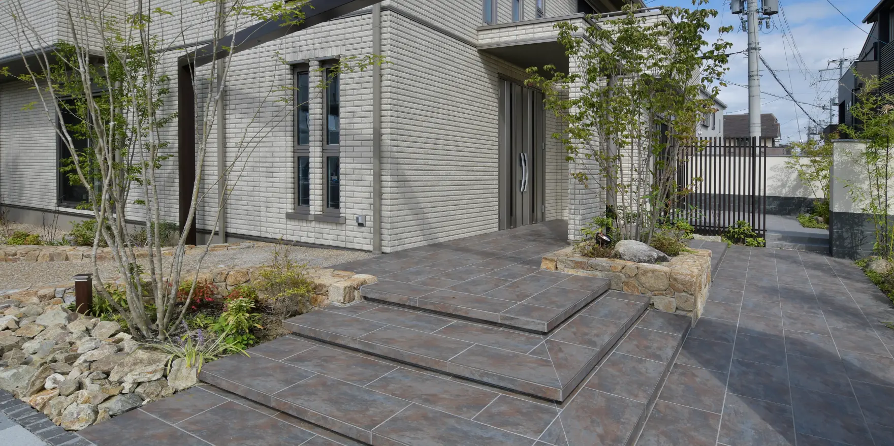 玄関へと続く広いタイル階段と、自然石を積んだ花壇や植栽の外構