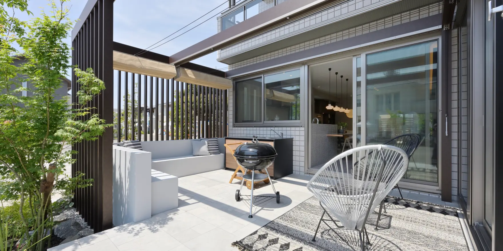 ホワイト基調の床タイルに、簡易キッチンとグリルを備えたテラス風の外構