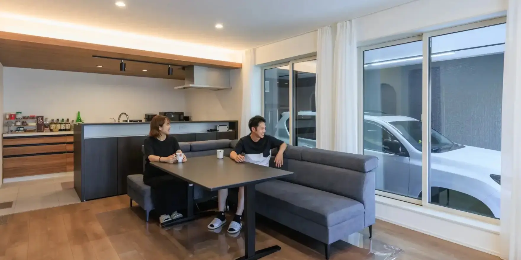 ご夫婦がリビングでくつろぎながらビルトインガレージの愛車を眺めている様子