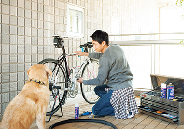 うちそとテラスで自転車のメンテナンスをする男性と犬